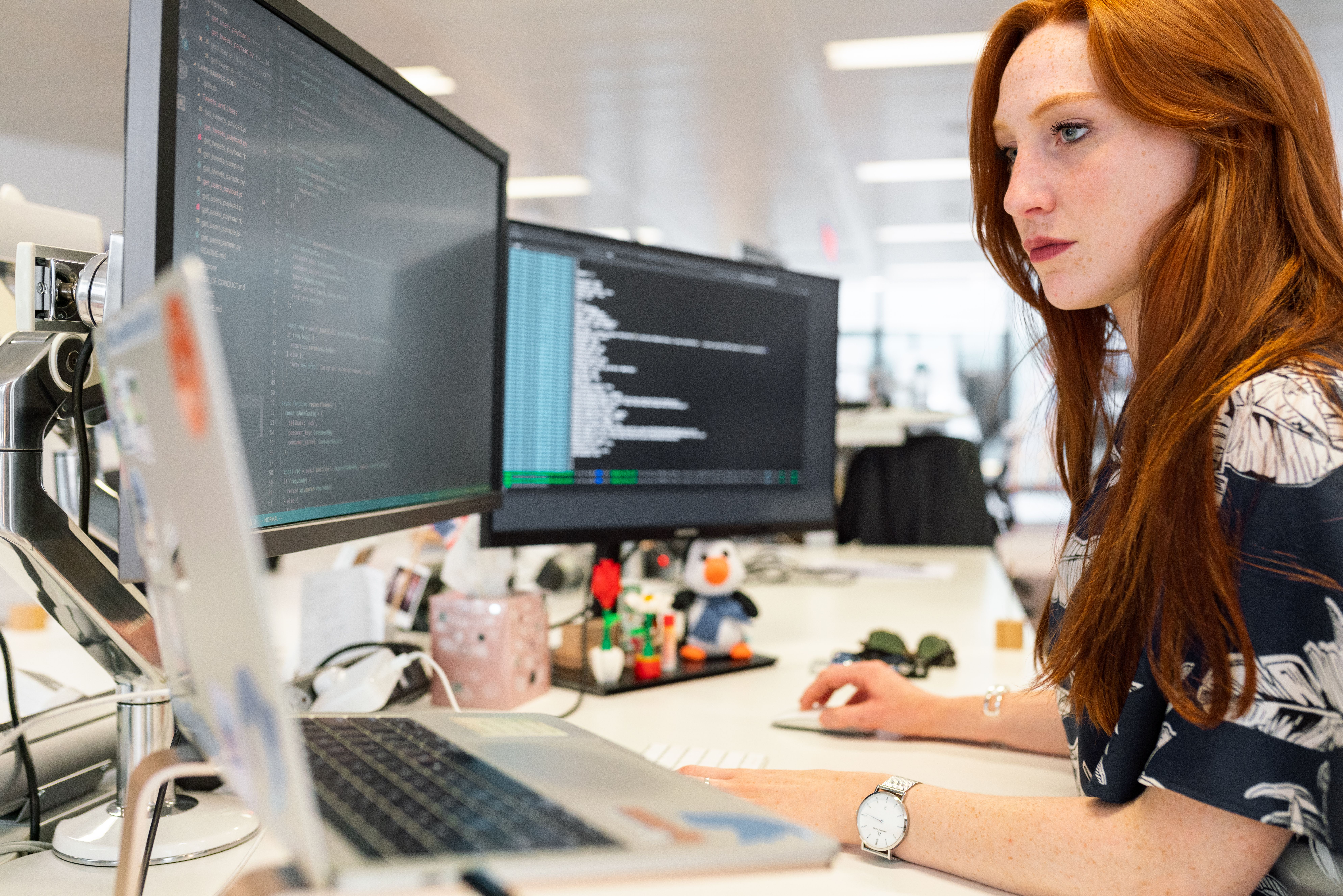 Software engineer coding at dual monitors in a modern office, suitable for a visual QA workflow.