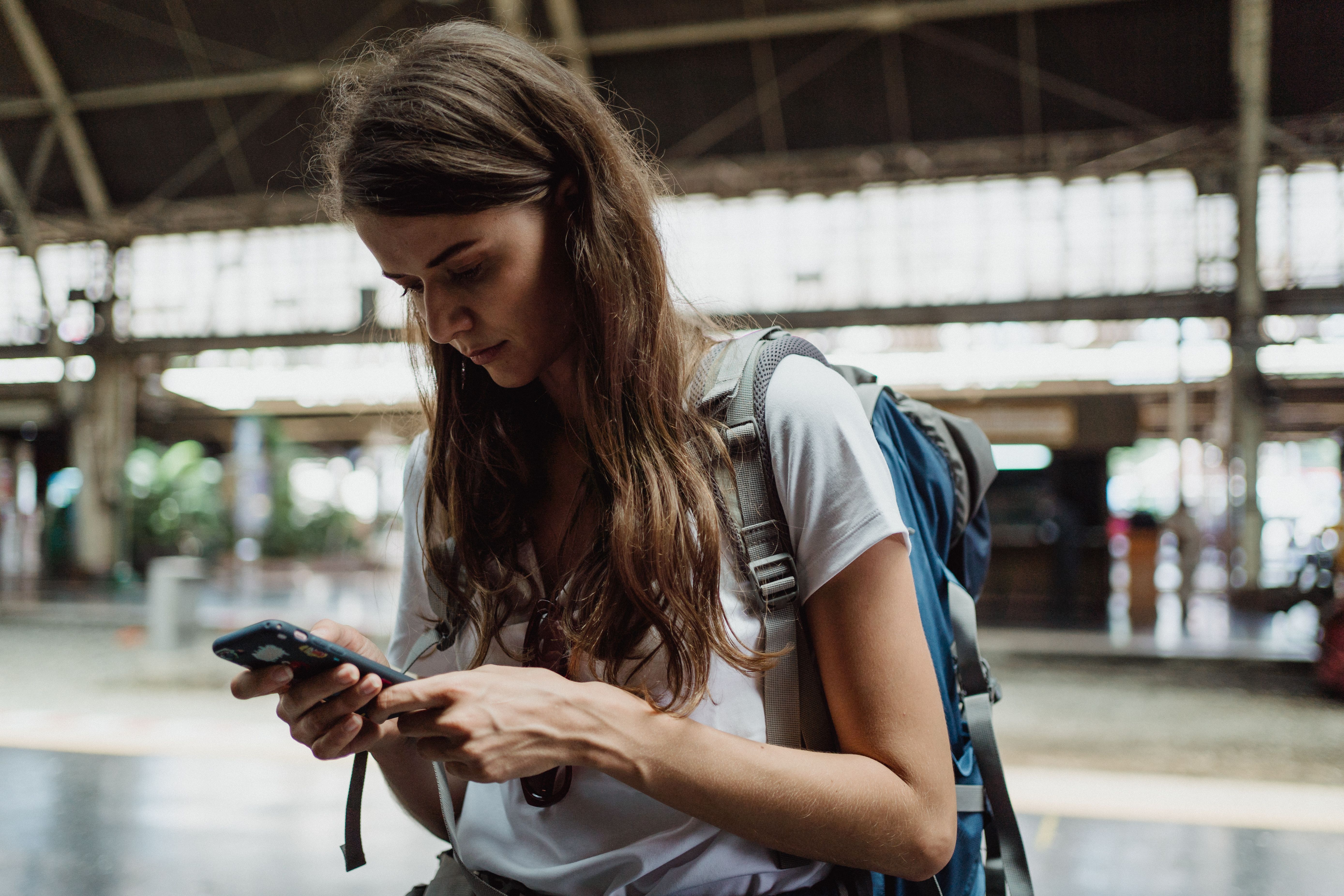 A young woman checks her smartphone while traveling at a train station